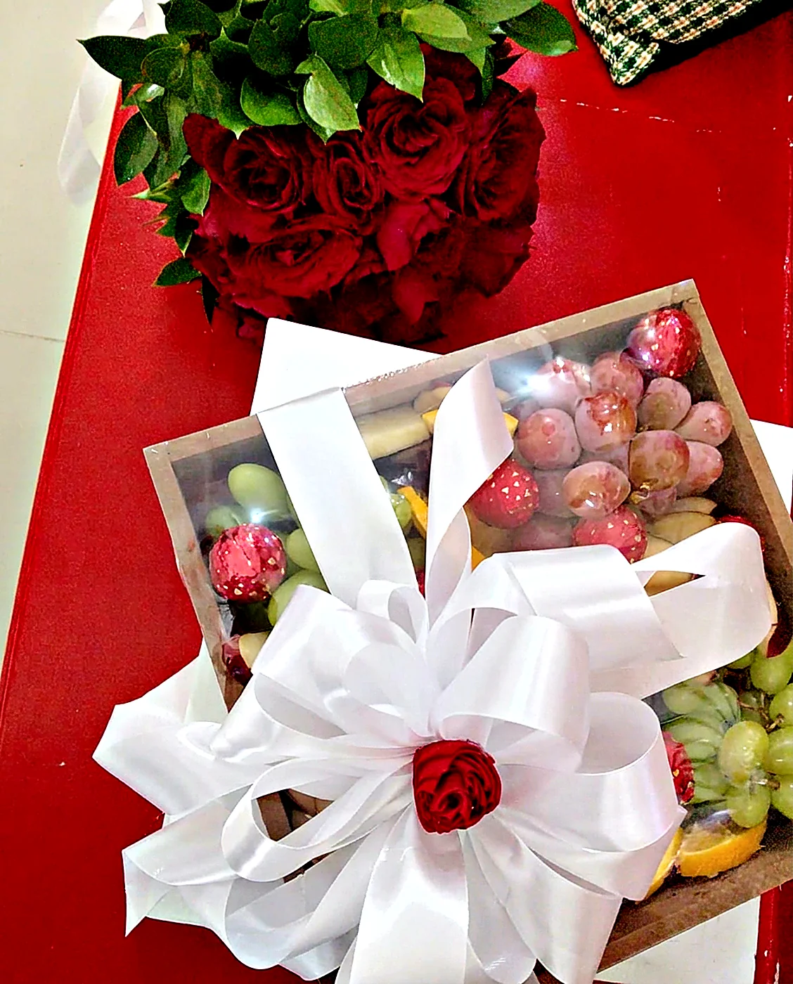 Caja con frutas y fresas, lazo blanco y rosas rojas
